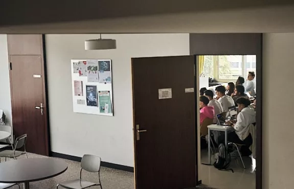 photo d'un couloir d'école avec une porte ouverte où on voit les étudiants dans la classe 