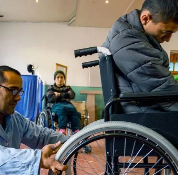 Personne en fauteuil roulant avec quelqu'un derrière qui semble réparer le fauteuil