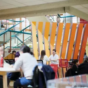 Des étudiants discutent autour de tables hautes dans le hall d'entrée de la HEdS-Genève