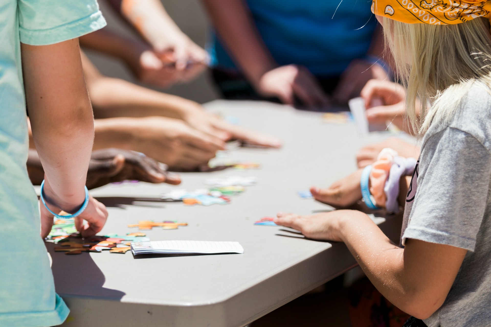 Photo de dos d'un adulte et un enfant qui prennent des pièces de puzzle sur une table. En arrièe plan légèrement flouté, on voit les mains de 5 autres personnes qui sont aussi autour de la table et participent au puzzle.