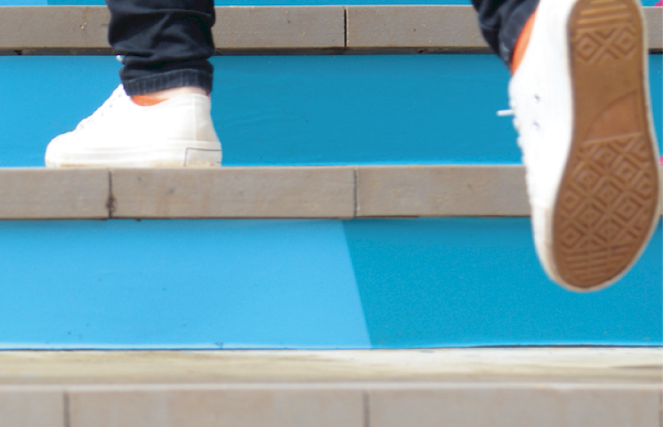 Image d'un escalier bleu et un étudiant qui marche dont on ne voit que les pieds