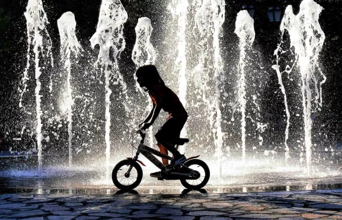 Photo de la silhouette d'un enfant à vélo devant des jets d'eau