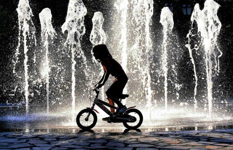 Photo de la silhouette d'un enfant à vélo devant des jets d'eau