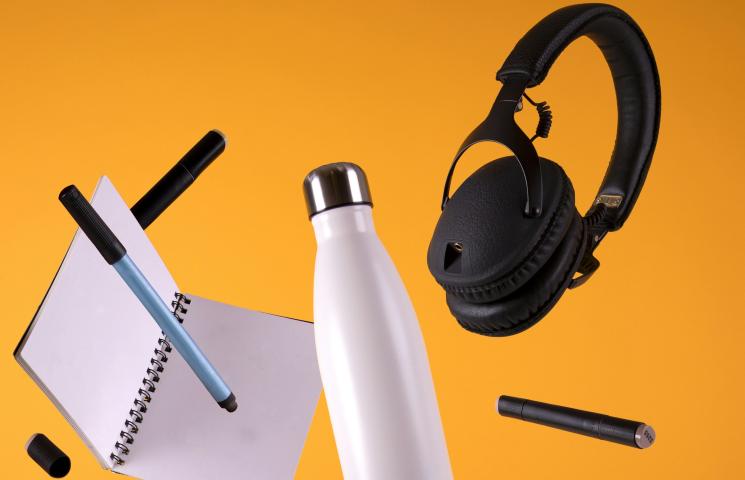 Une gourde, un casque audio, un carnet et des stylos flottent sur un fond jaune pétant.