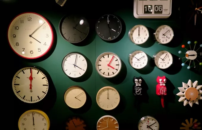 Photo d'un mur vert foncé recouvert d'une vingtaine d'horloges toutes différentes. Elles affichent toutes une heure différente, une majorité semble d'accord sur le fait qu'il est à peu près 16h.