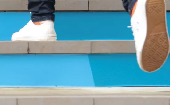 Image d'un escalier bleu et un étudiant qui marche dont on ne voit que les pieds